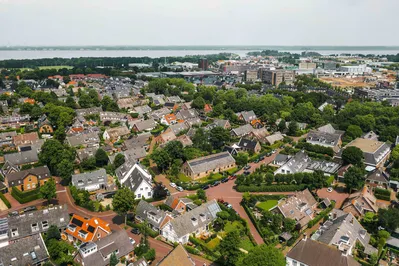 Luchtfoto van een woonwijk met groene tuinen en huizen, met een zicht op water in de achtergrond.