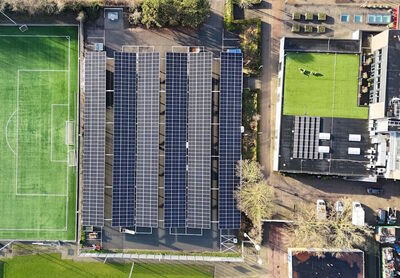 Luchtfoto van een sportveld met zonnepanelen op een nabijgelegen gebouw.