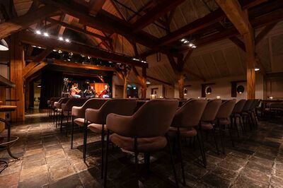 Interieur van een sfeervolle zaal met houten balken en stoelen, klaar voor een evenement of optreden.