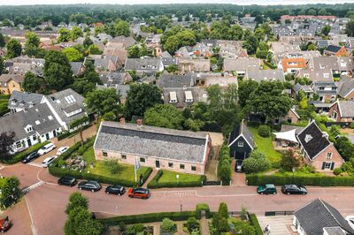 Luchtfoto van een woonwijk met huizen, tuinen en een rondweg in een groene omgeving.
